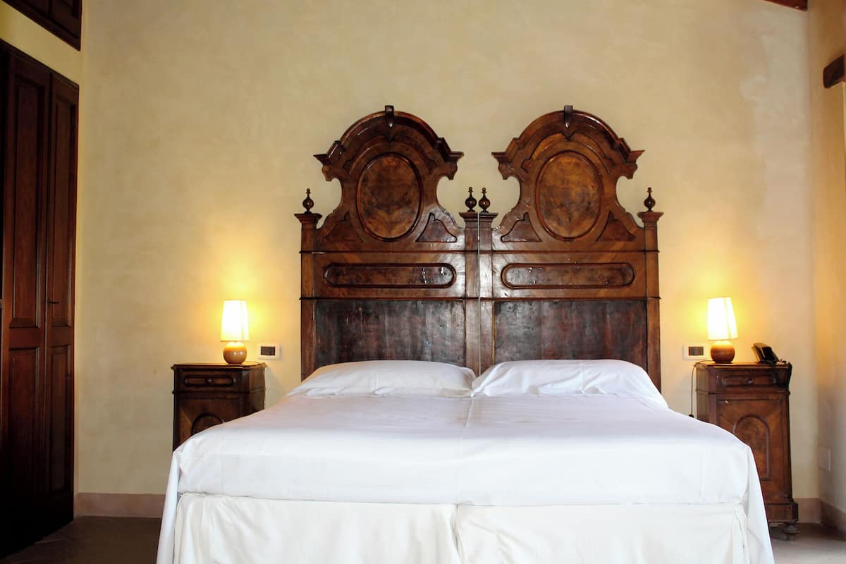 Een tweepersoonsbed met een houten hoofdbord, twee nachtkastjes met lampen en een houten garderobe.
