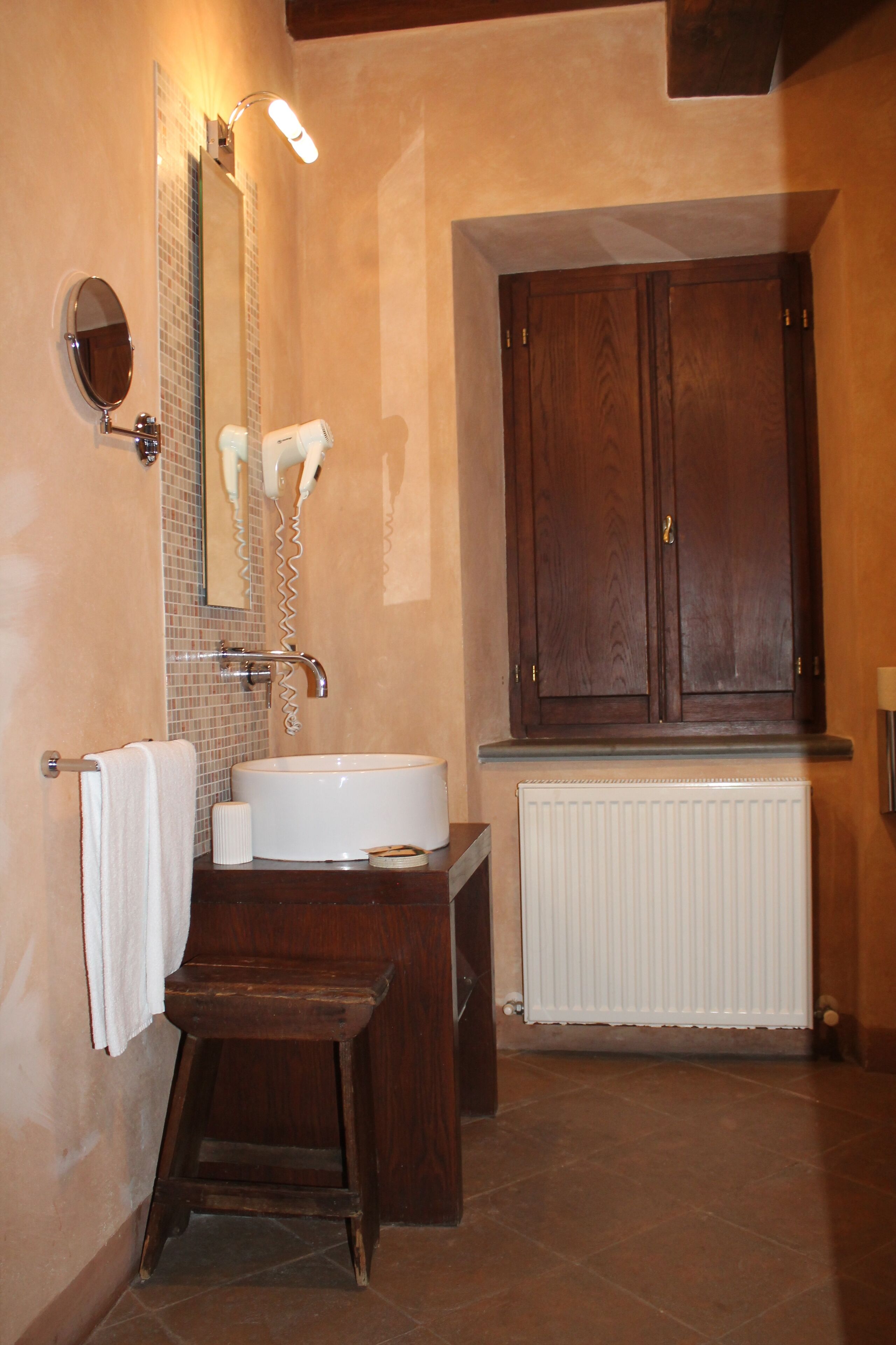Bagno con lavandino bianco, specchio, portasciuga, mobiletto in legno e termosifone.