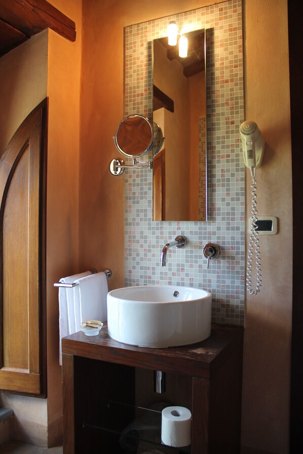 Un baño con tocador de madera, un lavabo blanco, un espejo, un secador de pelo y un dispensador de papel higiénico.