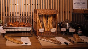 A bakery display with bread and pastries, a wicker basket, and a sign indicating the bakery's location. - Valpré Lyon Hôtel (Ecully)