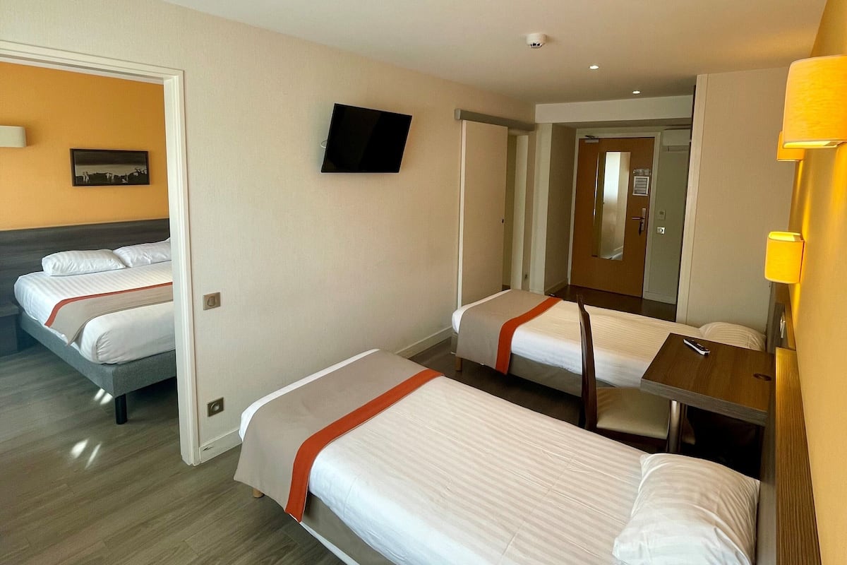 A hotel room with two single beds, a flat-screen TV, a wooden desk, and a mirror.