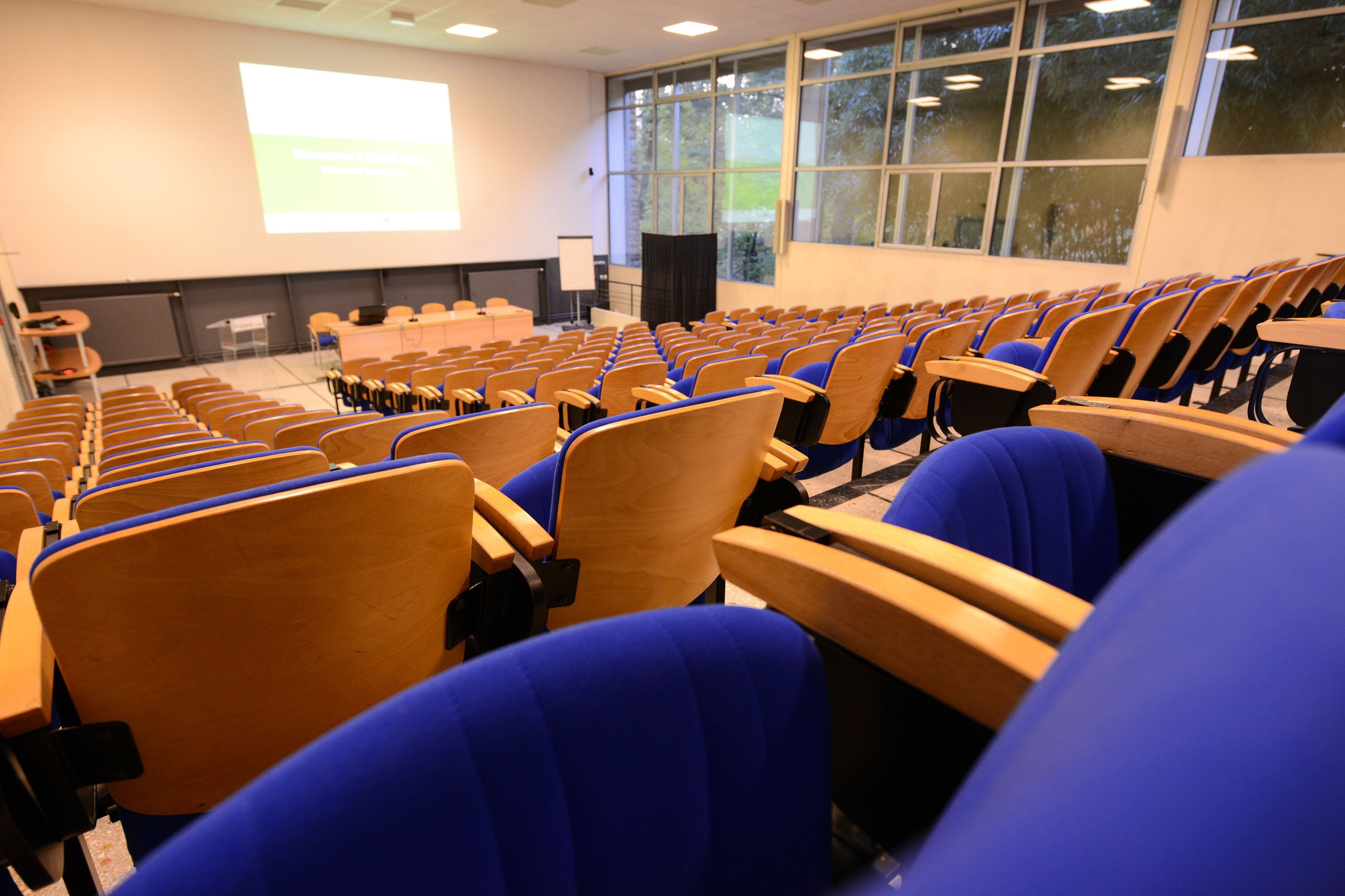 A lecture hall with rows of chairs, a projection screen, and a podium.