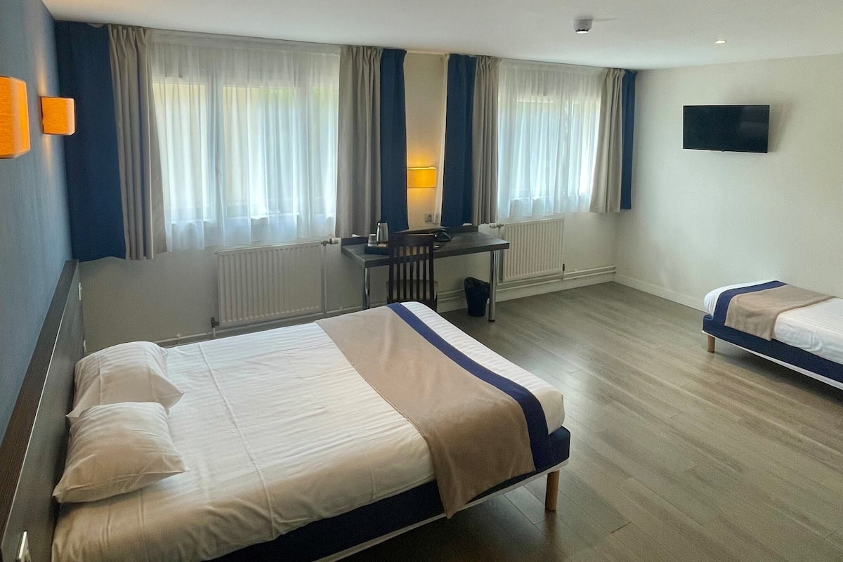 A hotel room with two beds, a desk, a chair, a TV, and a window with curtains.
