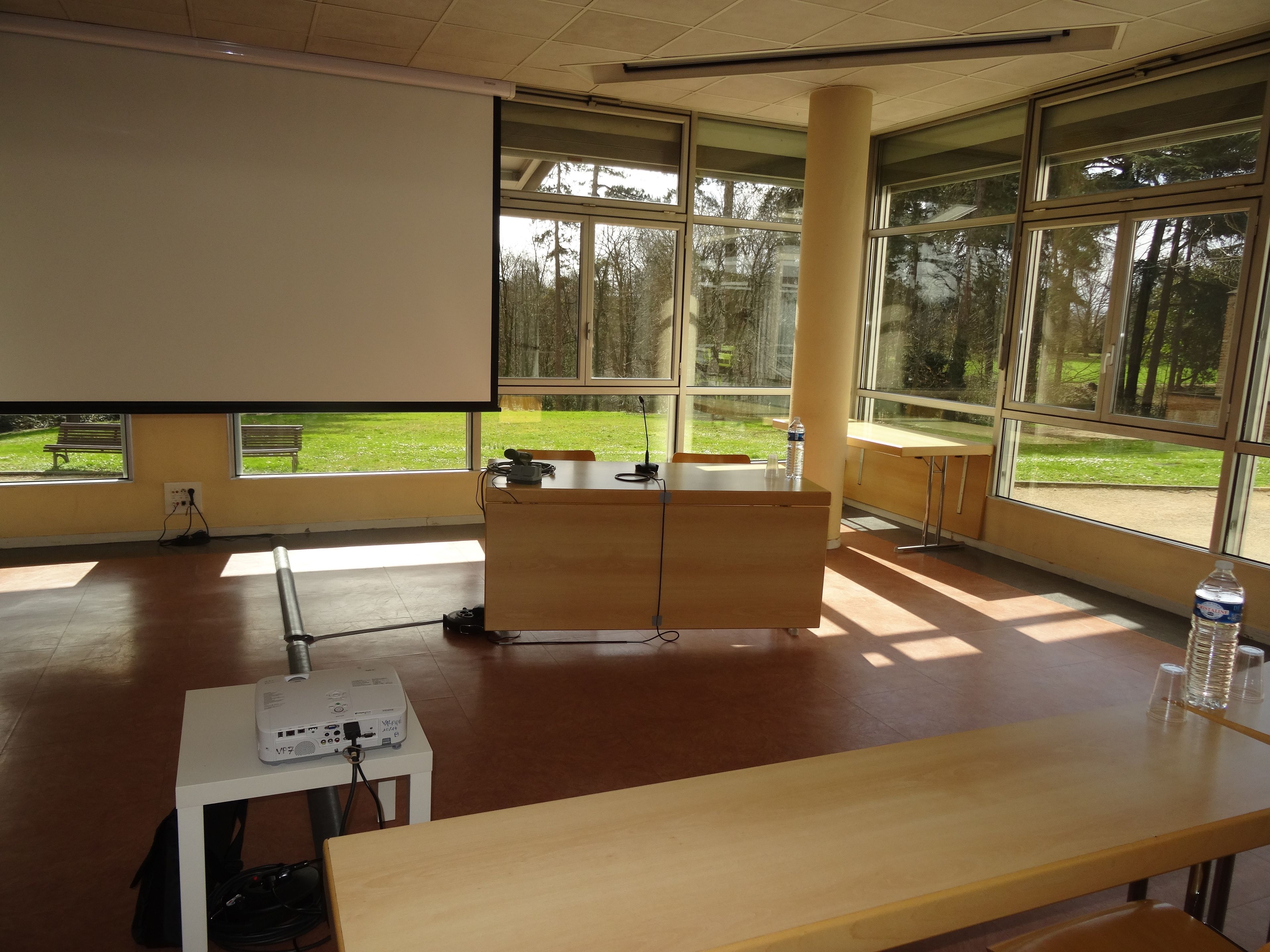 Un aula con un proyector, un pupitre de madera y un banco.
