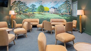 Une pièce avec des chaises et des tables de couleur beige, une fresque représentant un paysage tropical et deux lampadaires.