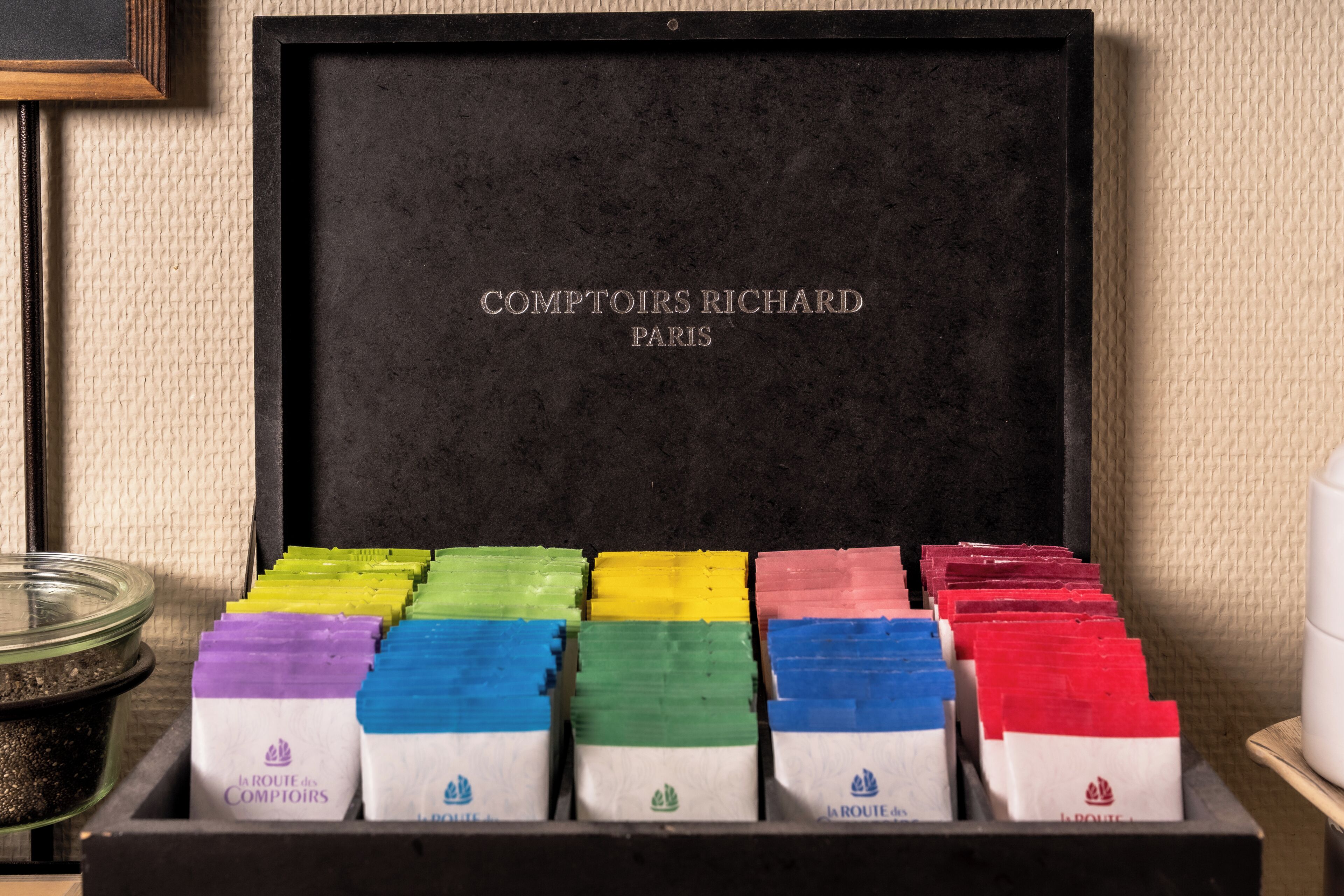 Una scatola nera con scomparti contenenti sacchetti di carta colorati con l'etichetta 'la ROUTE des COMPTOIRS'.
