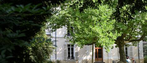 A building with a large tree in front, a pathway leading to the entrance, and a small outdoor seating area.