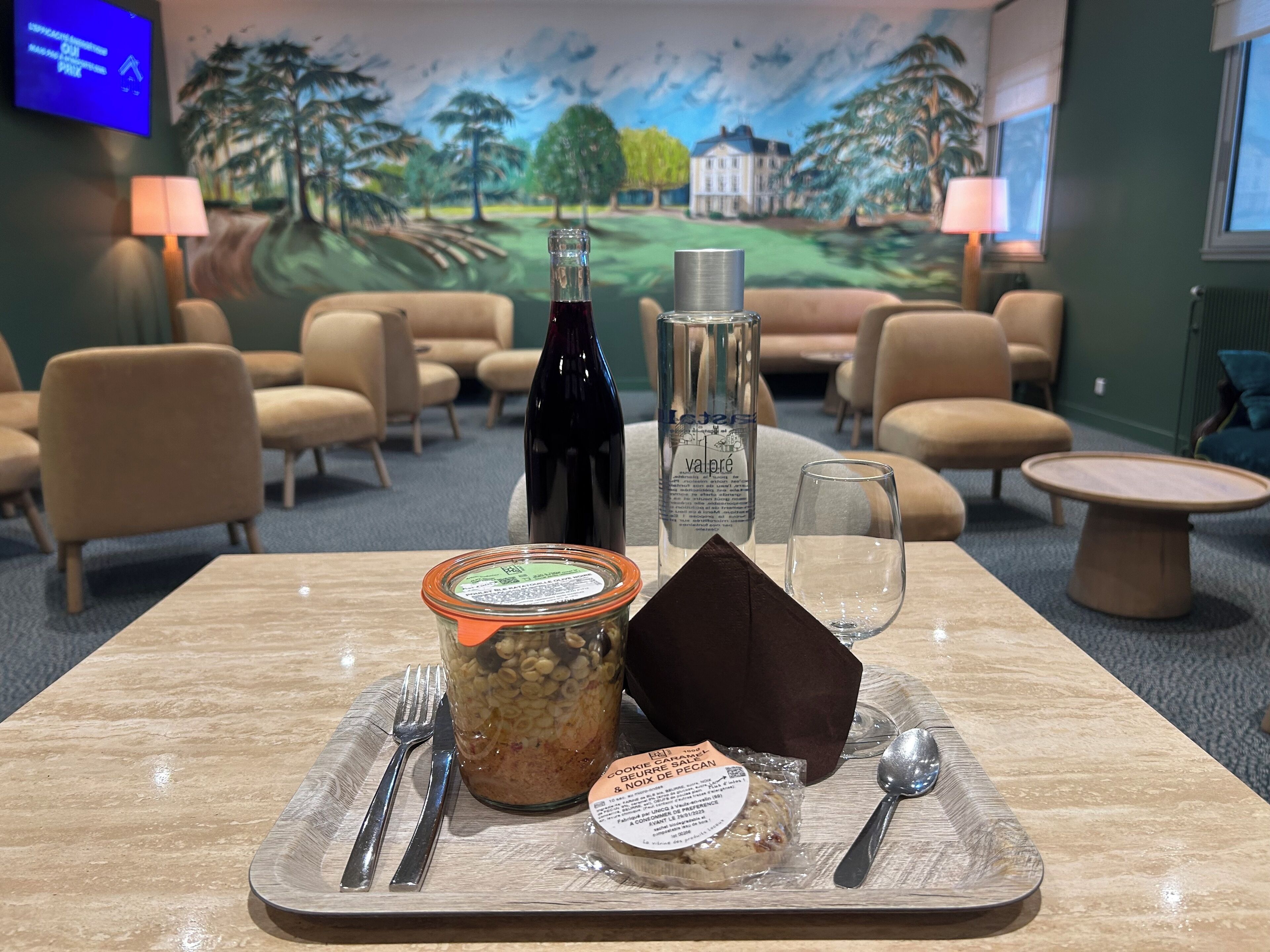 Une table à manger avec une bouteille de vin, un verre, un bocal de céréales et un paquet de biscuits.