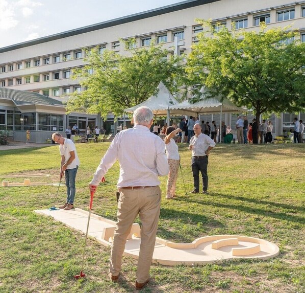 Un grupo de personas juega a croquet en un campo cubierto de césped, con un edificio moderno al fondo.