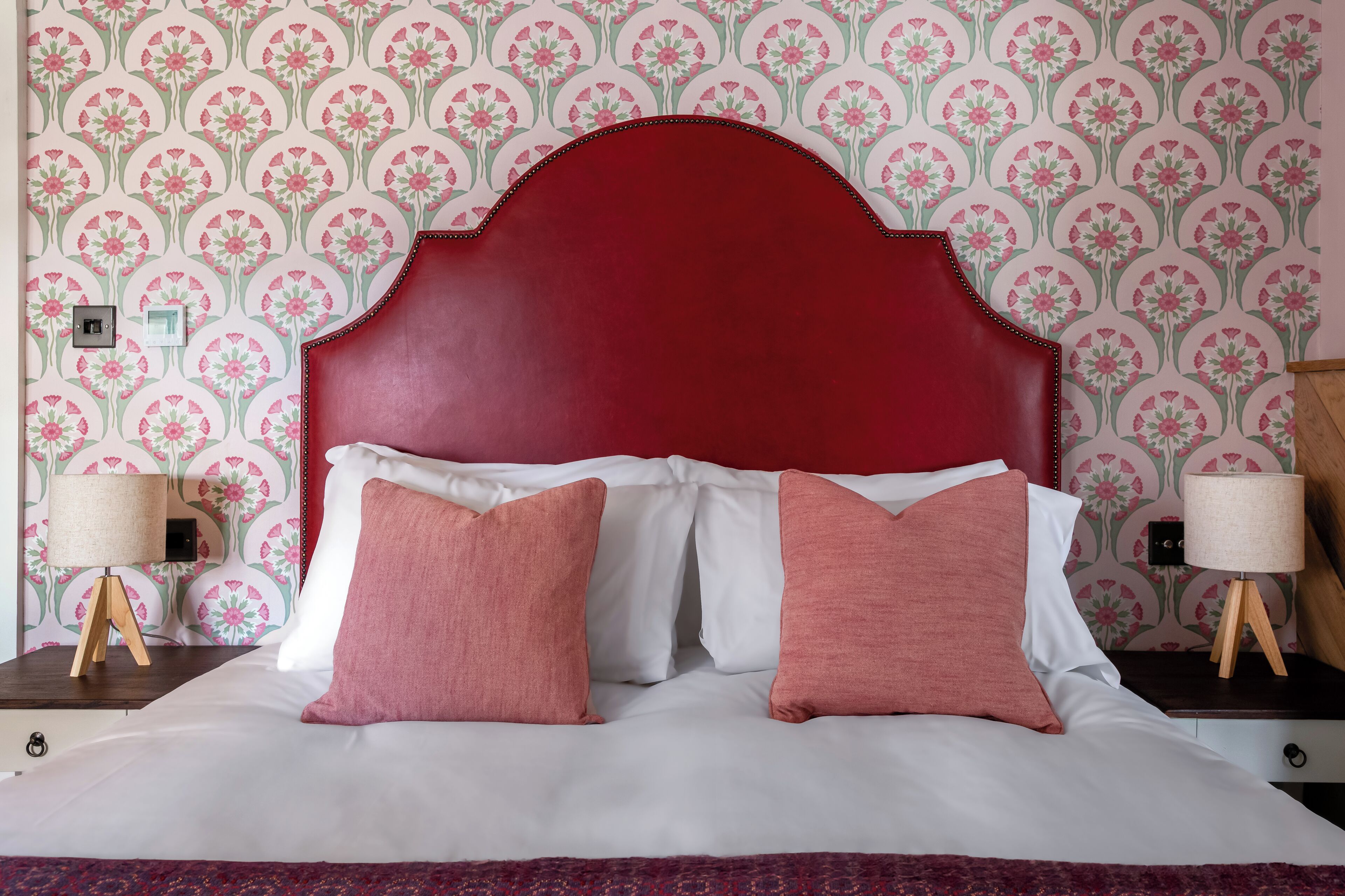 Una cama con cabecera roja, ropa de cama blanca y dos almohadas rosas.