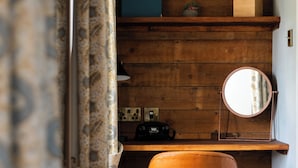 Ein Zimmer mit einem Holztisch, einem Stuhl, einem Spiegel und einem Regal mit einer Kiste und einer kleinen Pflanze.