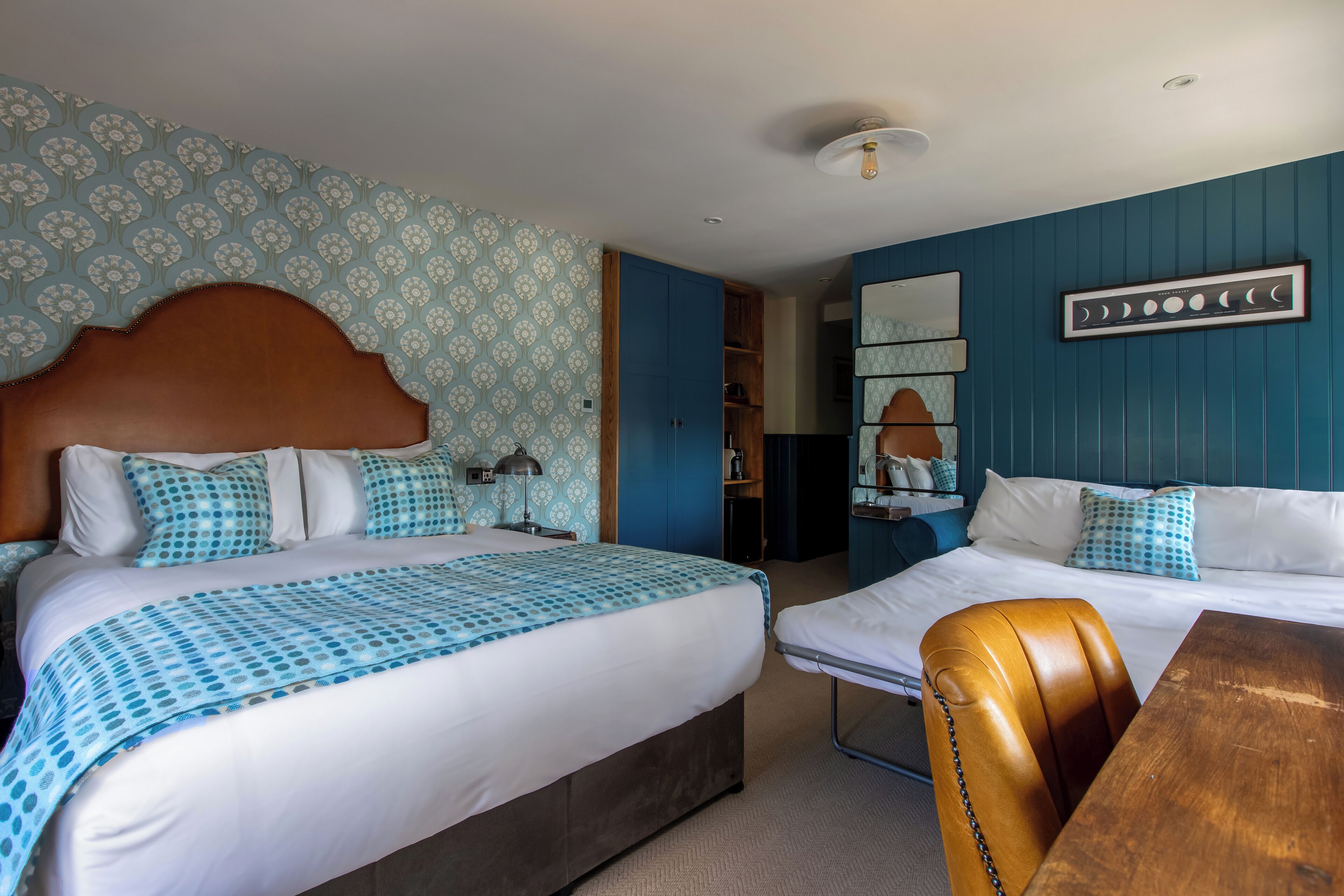A hotel room with two beds, a wooden headboard, a blue and white patterned bedspread, and a wooden table.
