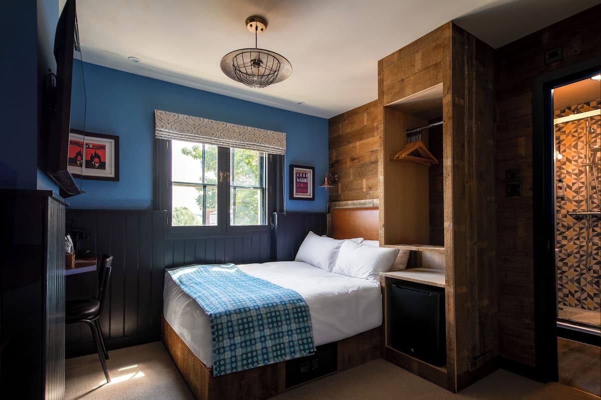A bedroom with a bed, a desk, a chair, a TV, and a window.