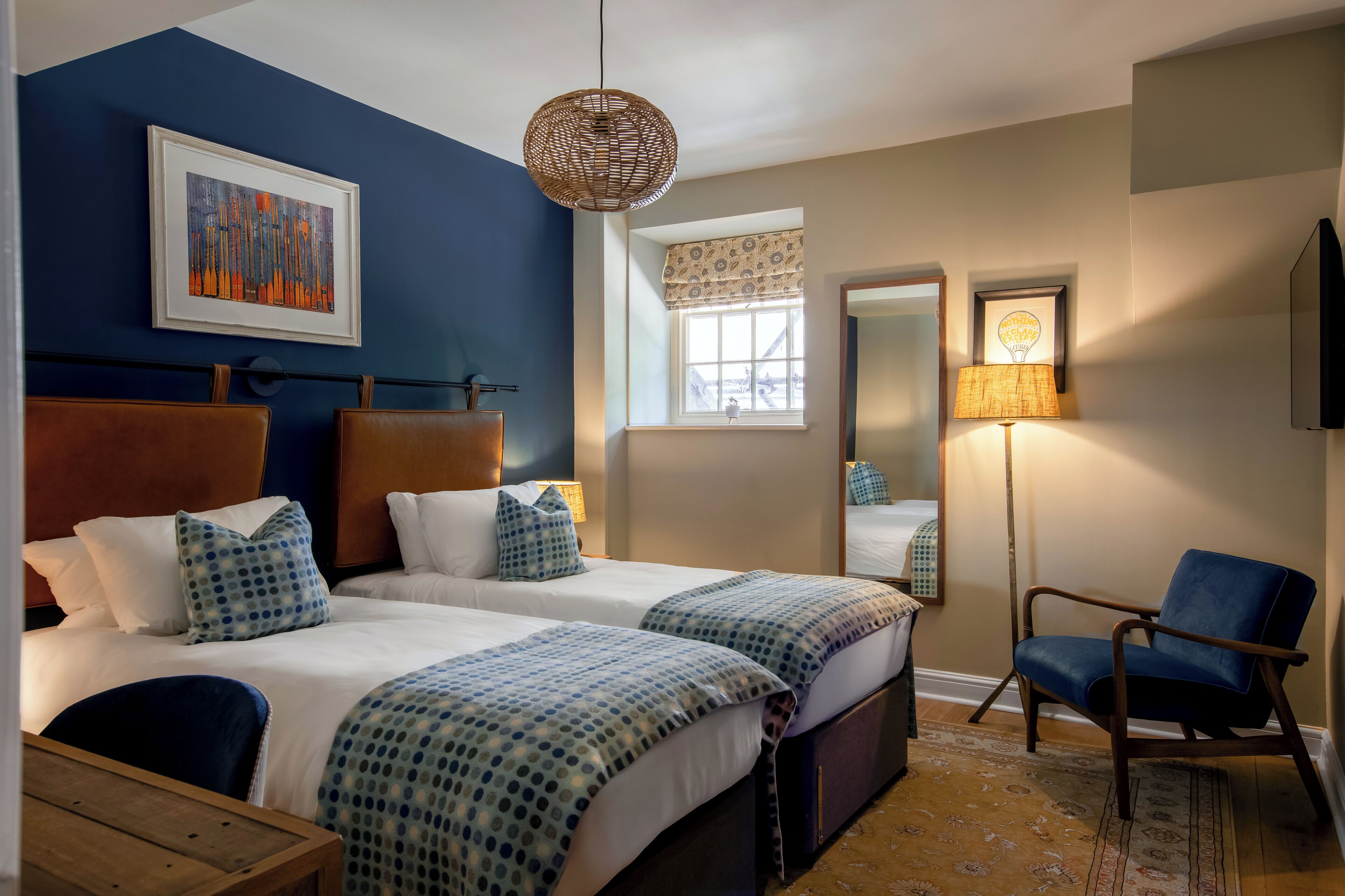Une chambre d’hôtel avec deux lits, une grande fenêtre donnant sur un beau paysage, un luminaire suspendu et une chaise.