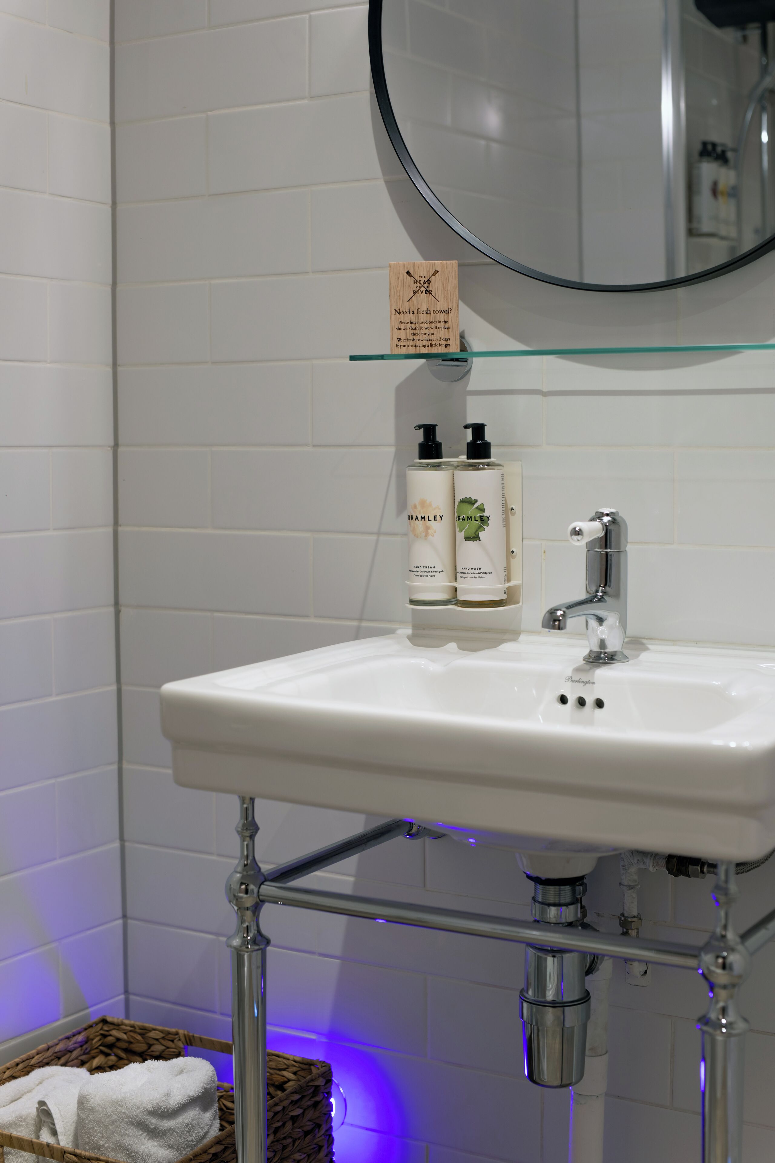 Un baño con un lavamanos blanco, dos botellas de champú, un espejo y un cesto para toallas.