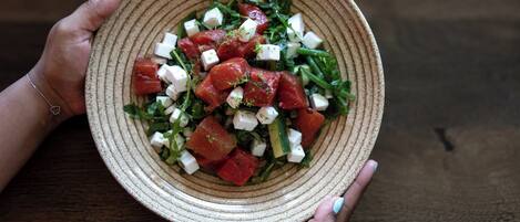 A person holding a bowl of salad with tomatoes, cucumbers, and cheese.