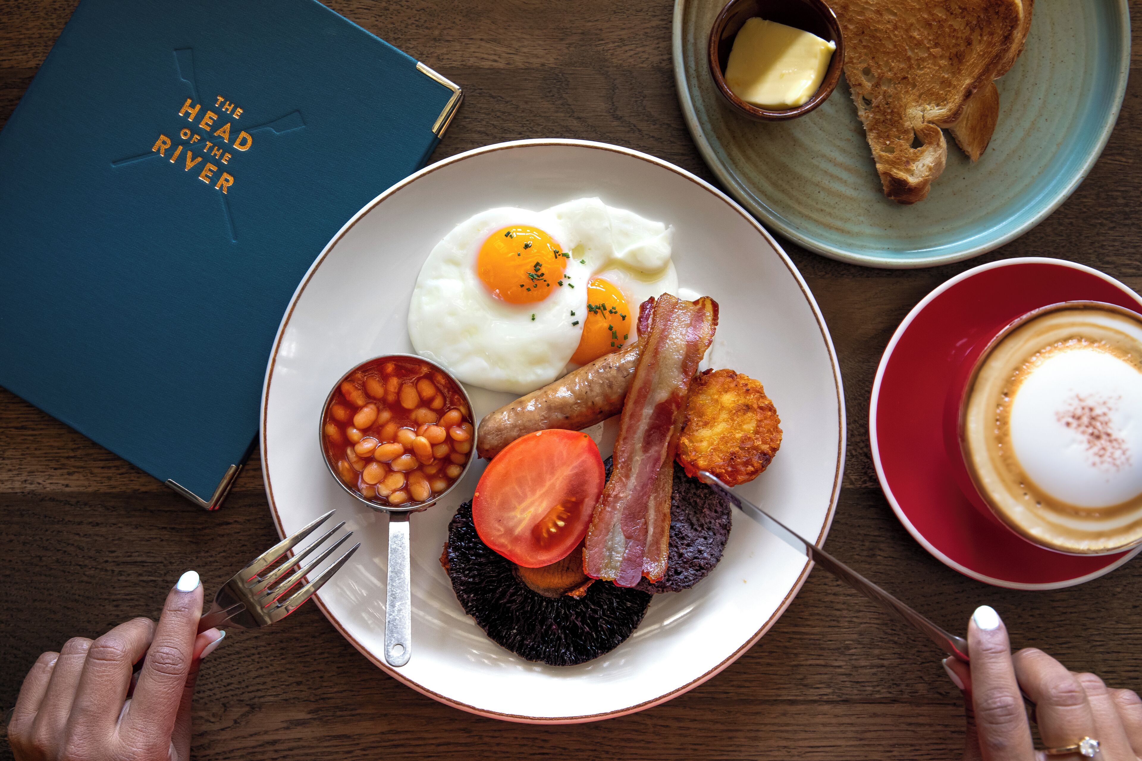 A breakfast plate with eggs, bacon, beans, and tomato, accompanied by toast and coffee.