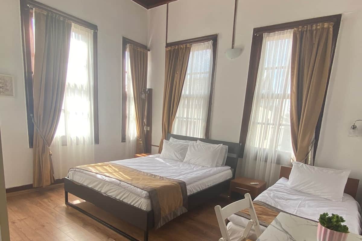 A hotel room with two beds, wooden flooring, and large windows with curtains.