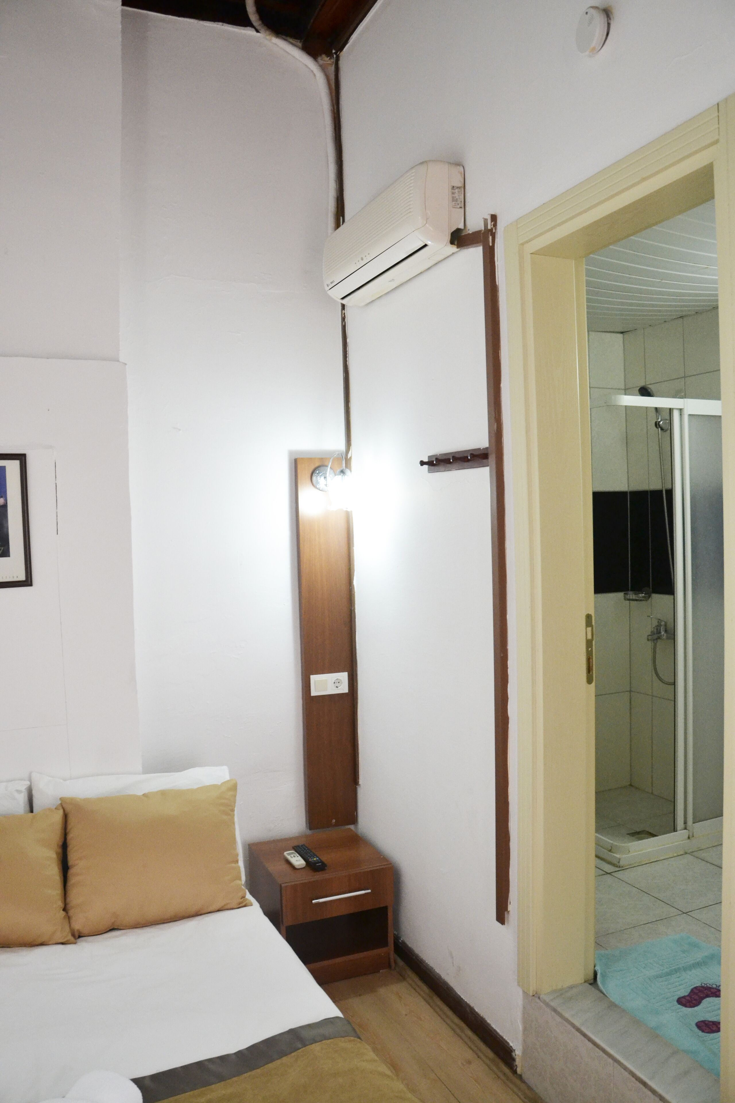 Habitación de hotel con cama, mesita de noche y unidad de aire acondicionado instalada en la pared.