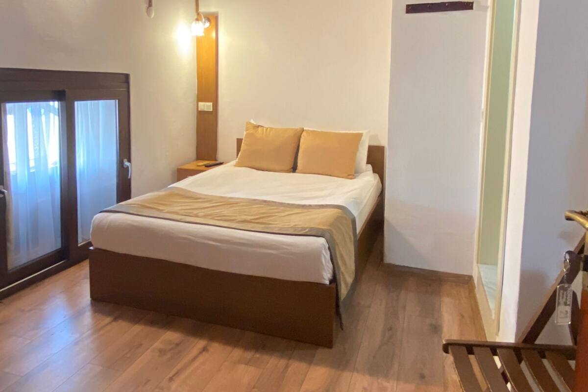 A bedroom with a wooden floor, a bed with beige bedding, a nightstand, a bench, and a sliding door.
