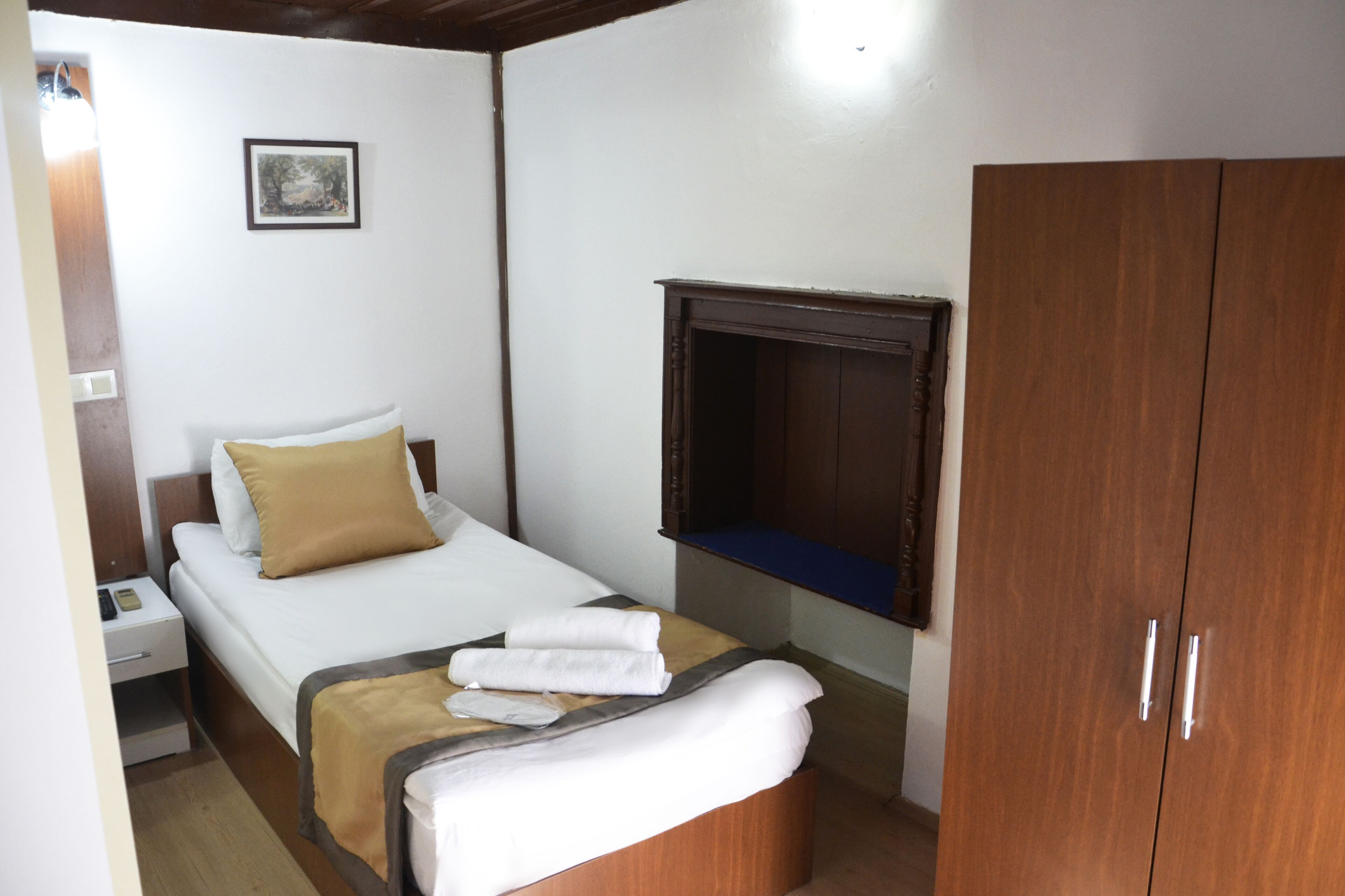 A hotel room with a bed, a wooden wardrobe, a nightstand, a bedside table, and a wall-mounted TV.