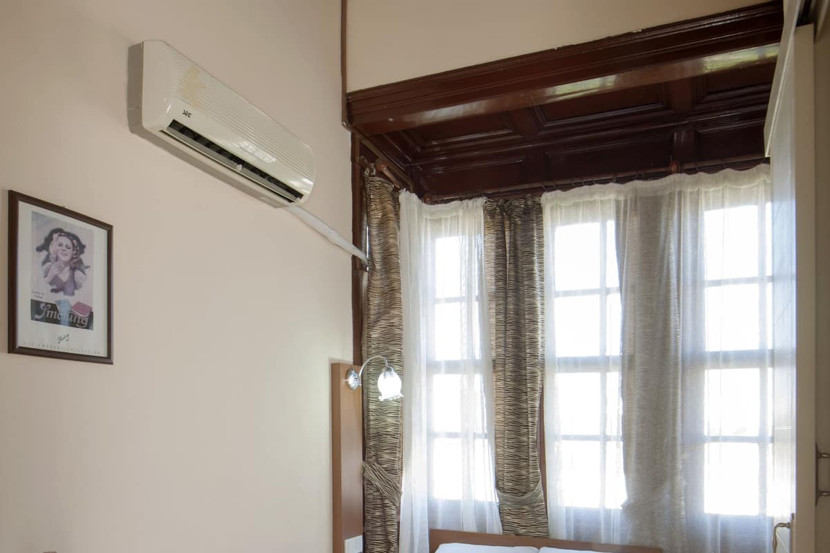 A bedroom with a bed, an air conditioning unit, a bedside table with a bottle and glasses, and a framed picture on the wall.