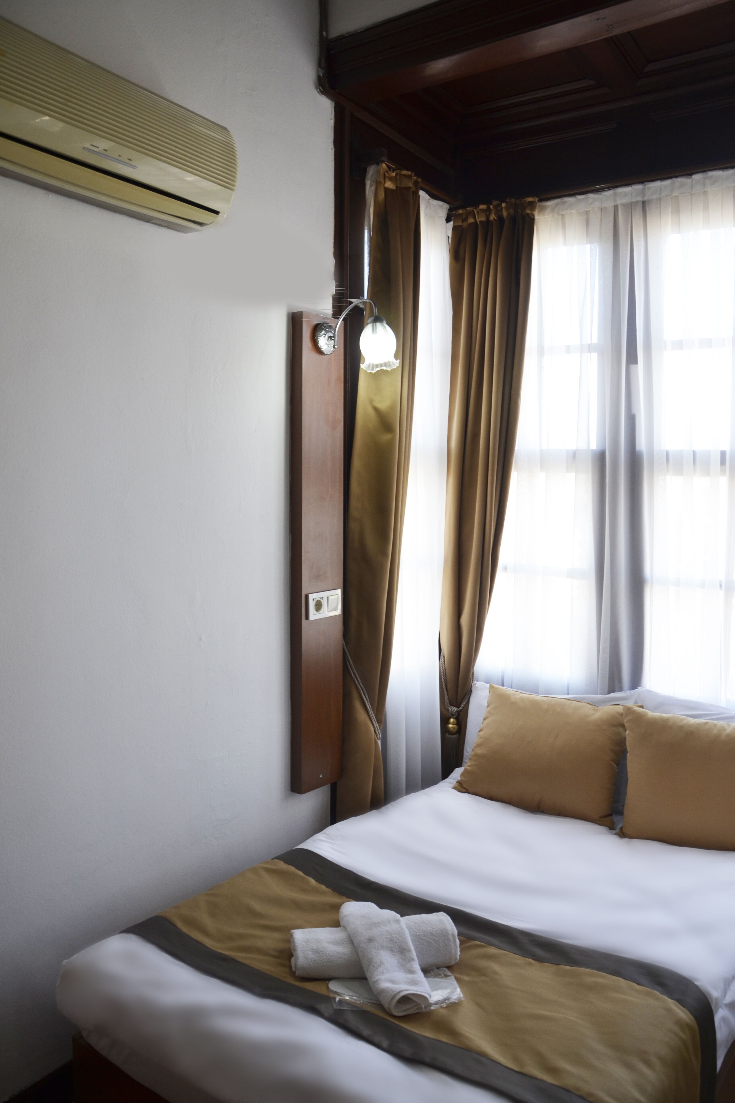 Habitación de hotel con cama, aire acondicionado de pared, ventana con cortinas e iluminación.
