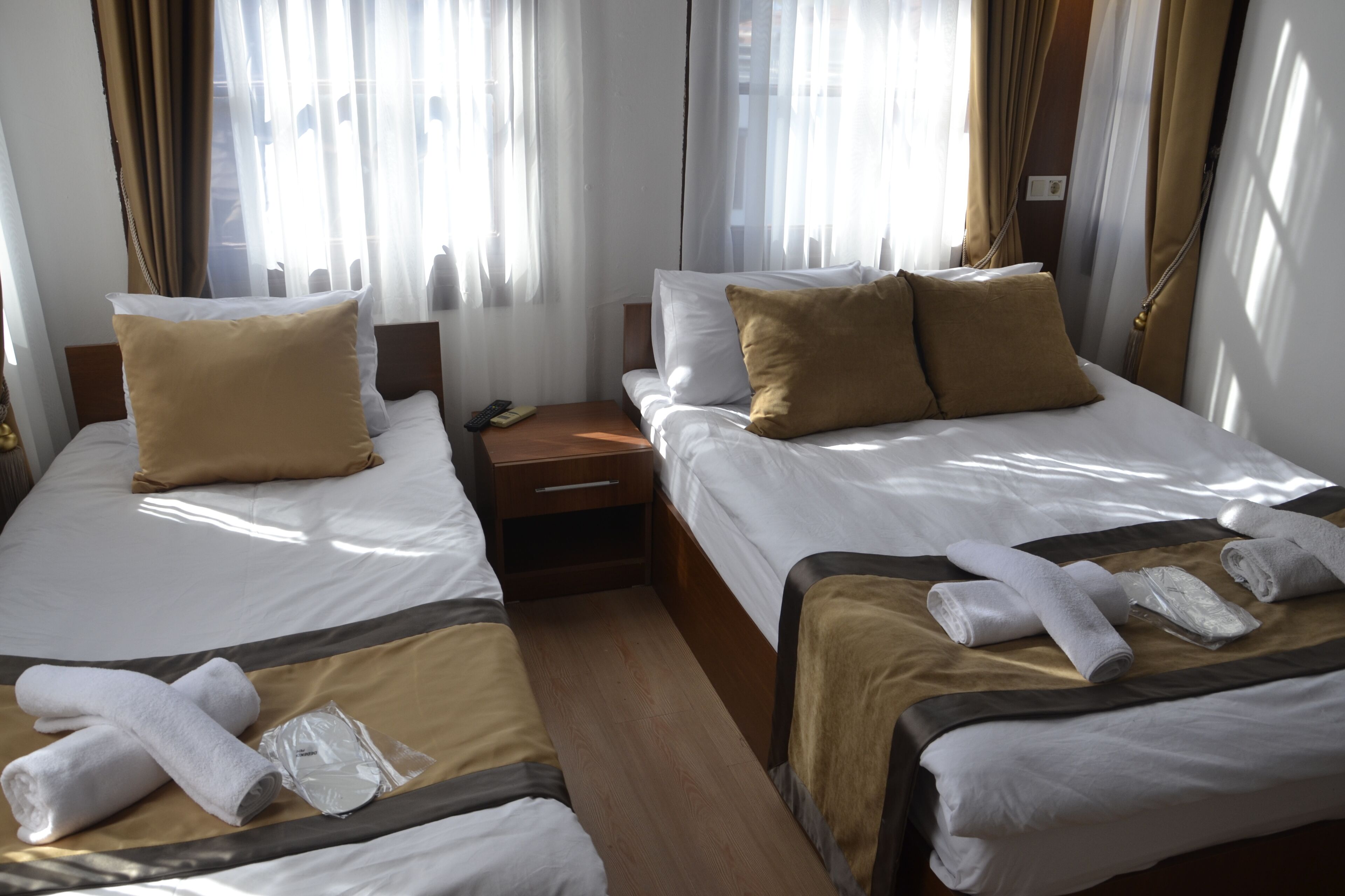 A hotel room with two single beds, each with a brown headboard, white bedding, and a brown accent pillow. There are towels and a remote control on the nightstand.