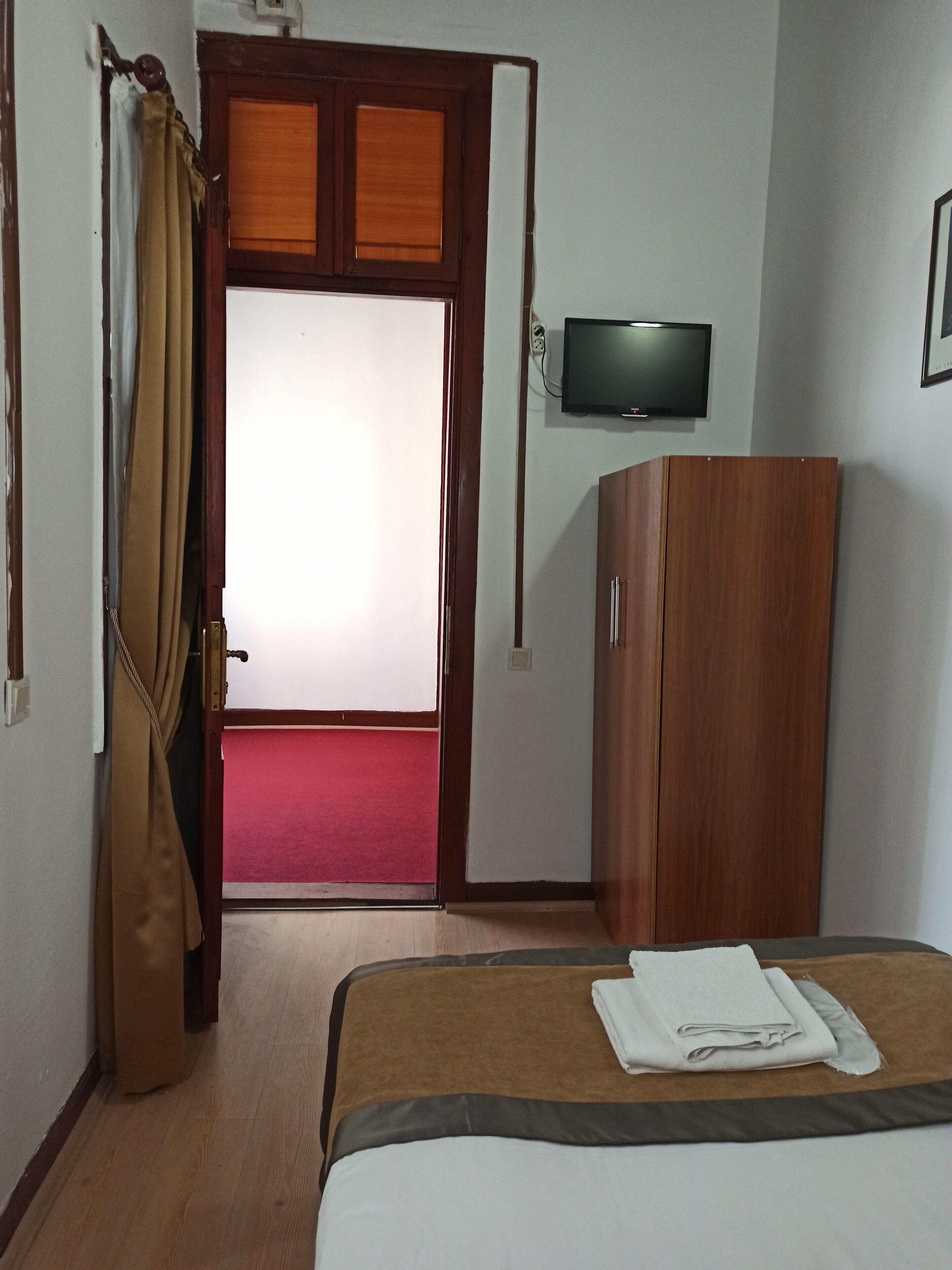 Een hotelkamer met een bed, een garderobe, een televisie en een deur naar een gebied met een rode tapijtvloer.