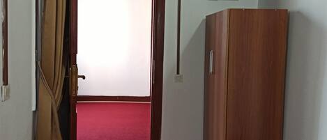 Een hotelkamer met een bed, een garderobe, een televisie en een deur naar een gebied met een rode tapijtvloer.