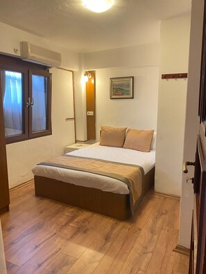 Une chambre à coucher avec un lit, un plancher en bois, une fenêtre avec des rideaux, un climatiseur fixé au mur et un tableau.