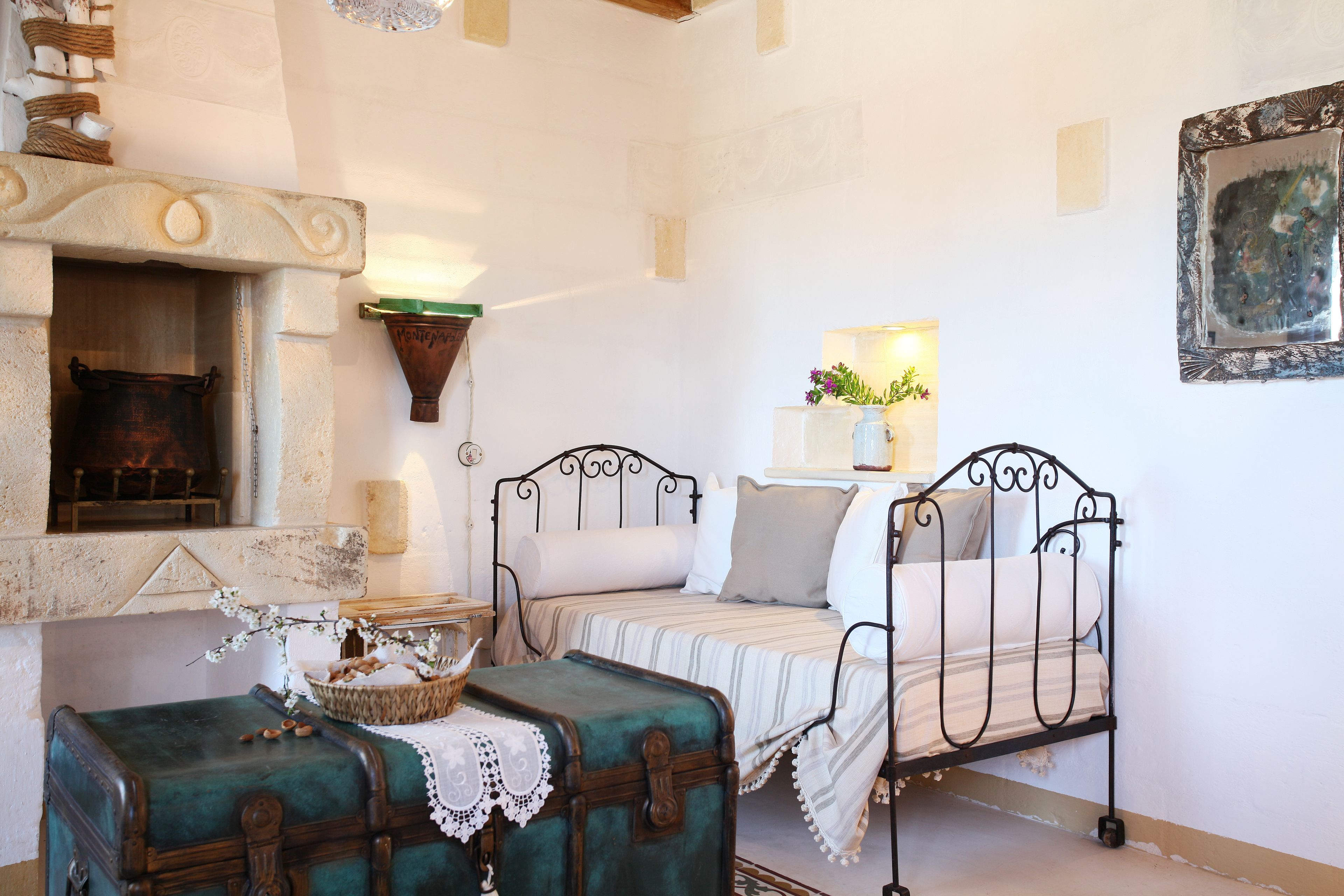 Um quarto aconchegante com lareira, uma cama com estrutura de metal, uma mala verde e uma cesta de pão.