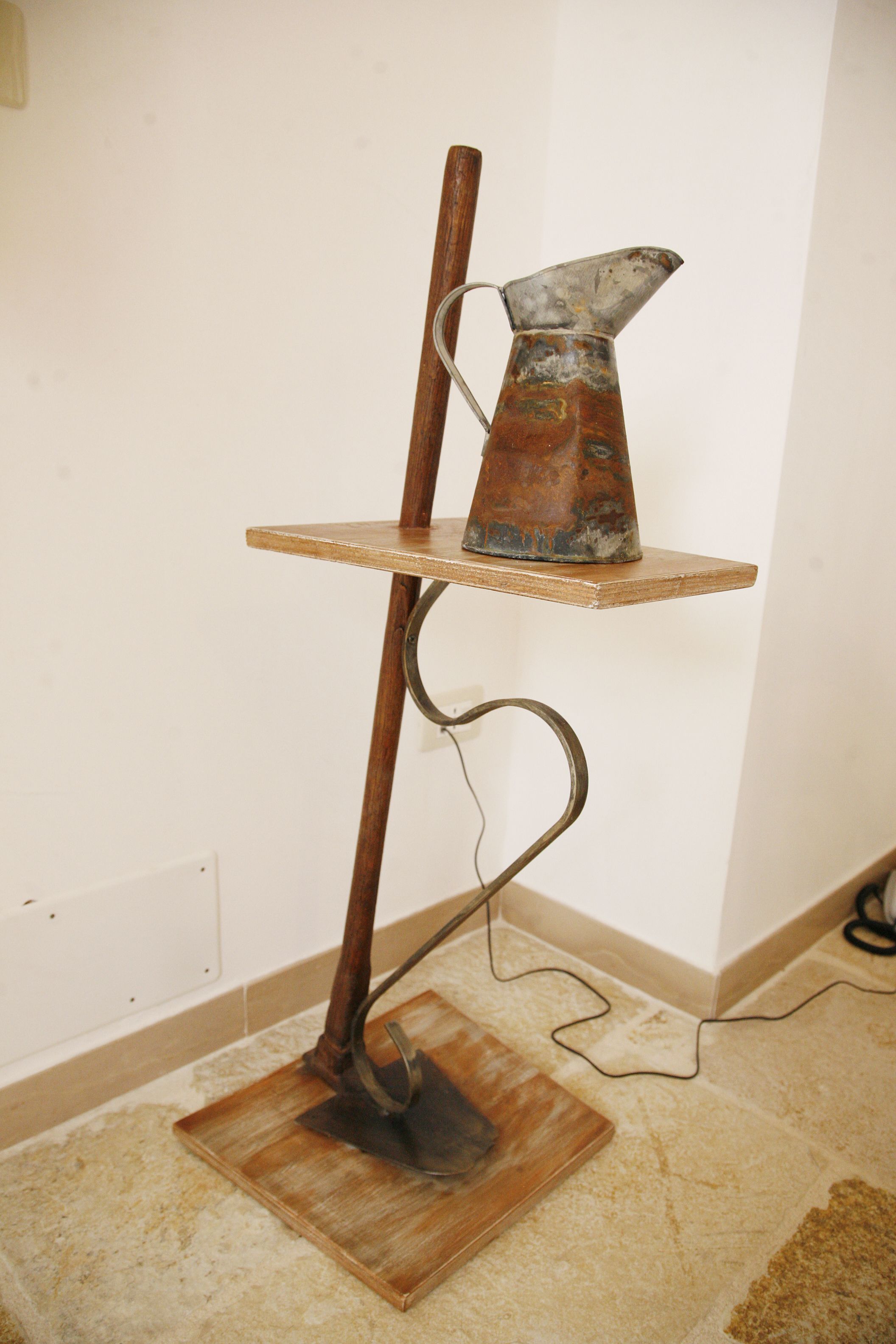 A metal sculpture with a wooden base and a metal pitcher on a shelf.