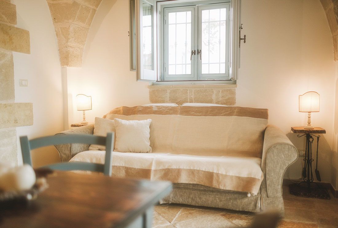 A cozy room with a stone wall, a wooden table, a cushioned sofa, and a window with a view.