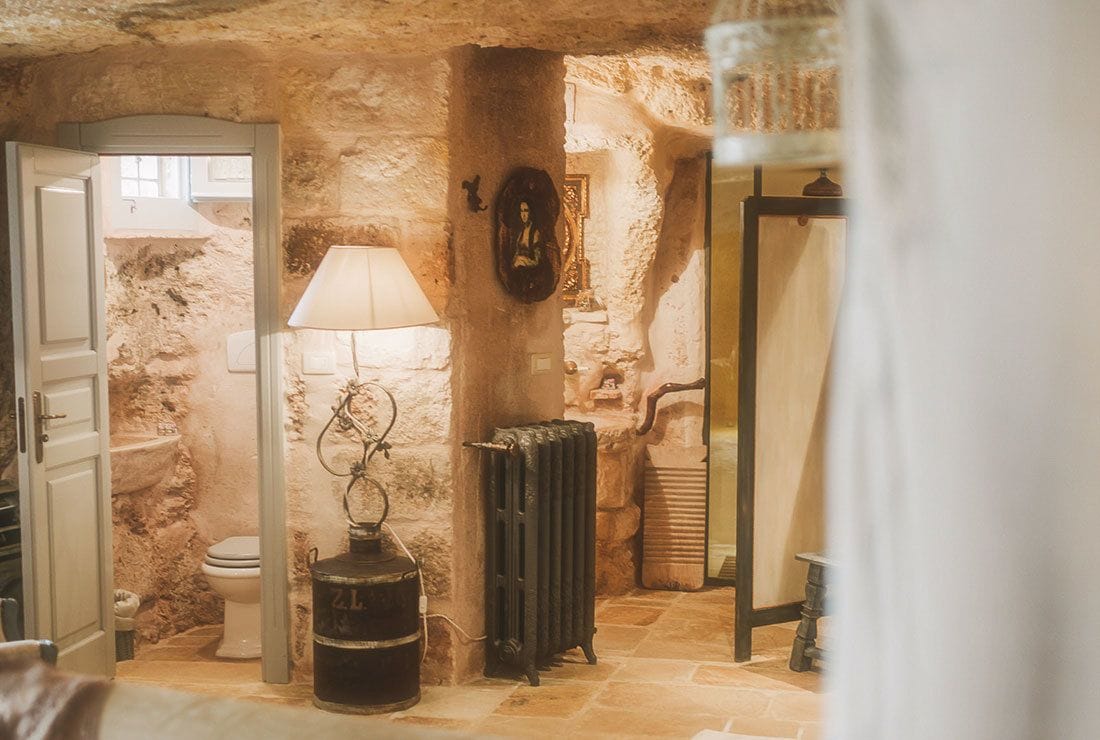 A rustic bathroom with a stone wall, a radiator, a wooden barrel, and a toilet.