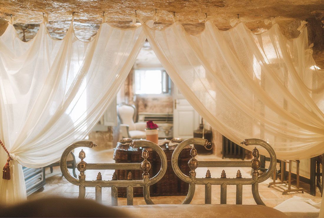 A room with a bed covered by sheer white curtains, a vintage metal bed frame, and a rustic wooden headboard.