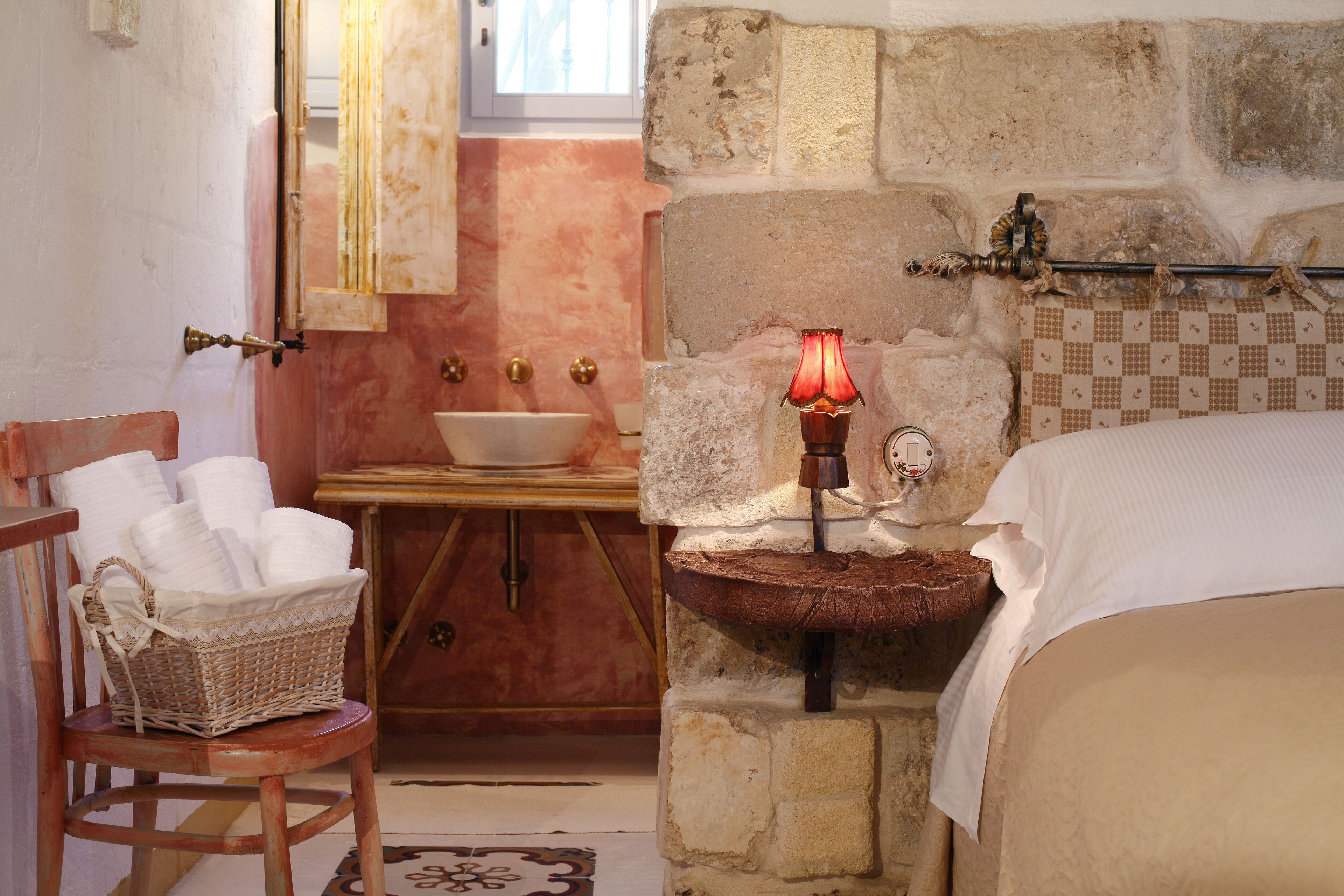 A bathroom with a stone wall, a wooden chair with a basket, a sink, and a bed.