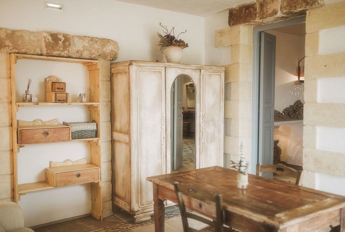 Une pièce rustique avec une table et des chaises en bois, un meuble blanc avec un miroir, et une arche en pierre.