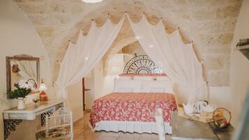 Un dormitorio con techo de piedra, cama con dosel, mesita de noche con lámpara y espejo.