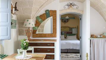Experience the warmth of this charming room, featuring a stone wall, arched doorway, and a beautifully appointed bed with a green headboard.