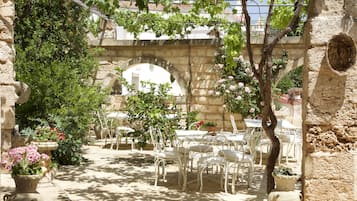 An outdoor patio with stone arches, white metal chairs, and potted plants.