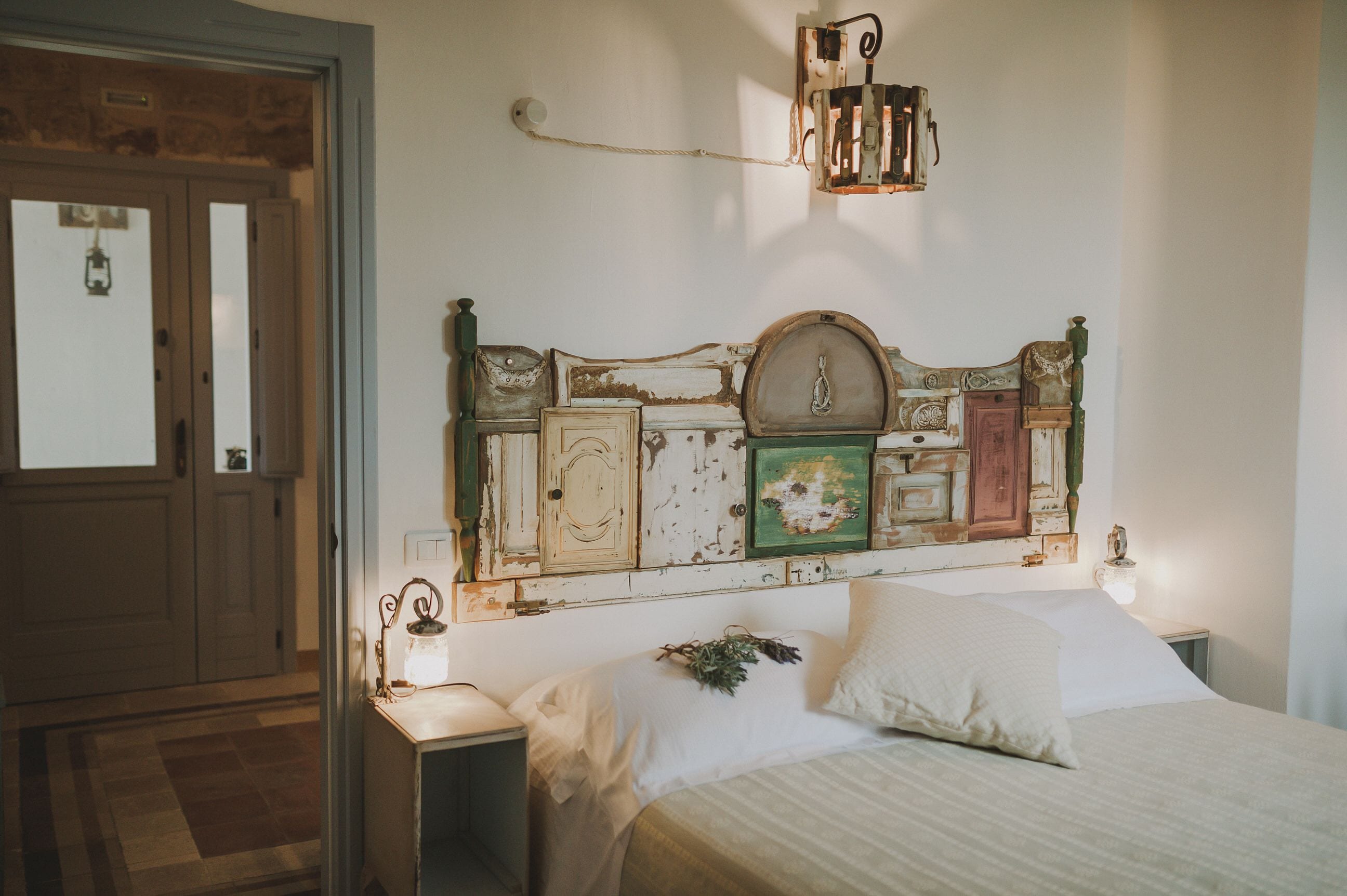 A bedroom with a rustic headboard, a bedside table with a lamp, and a door in the background.