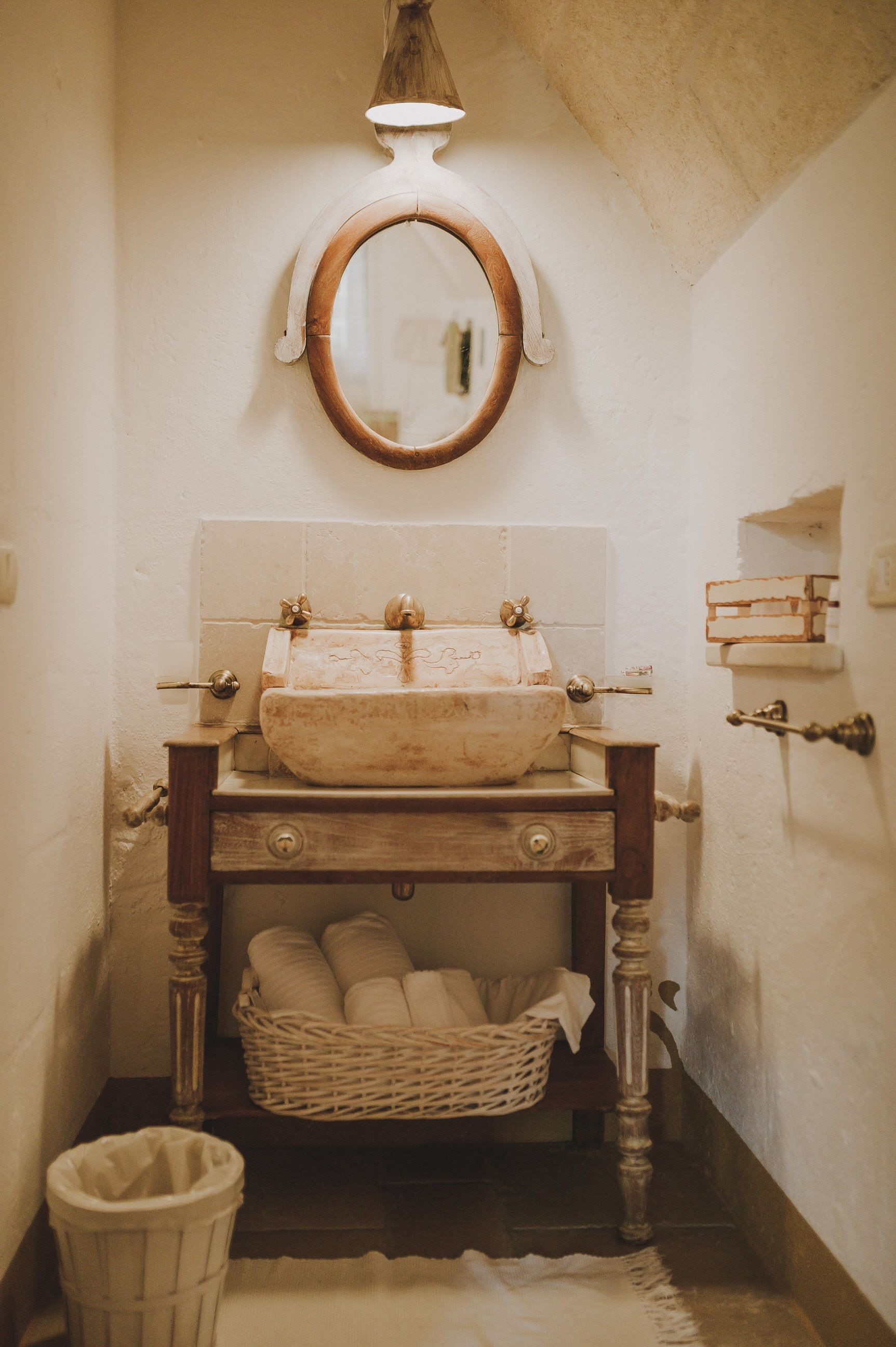 A narrow bathroom with a wooden vanity, a round mirror, and a sink with a vintage design.