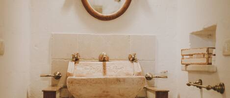 A narrow bathroom with a wooden vanity, a round mirror, and a sink with a vintage design.