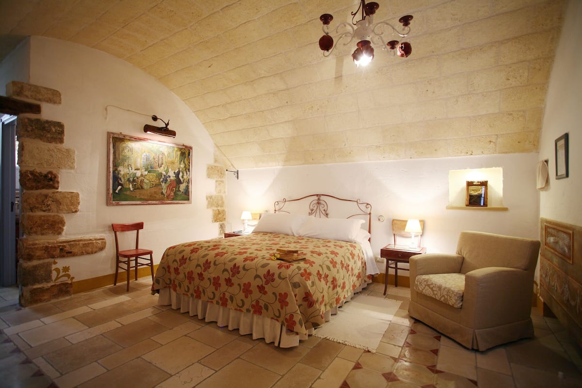 Ein Schlafzimmer mit Bett, Stuhl, Gemälde, einer Chandelieber und einer Steinwand.