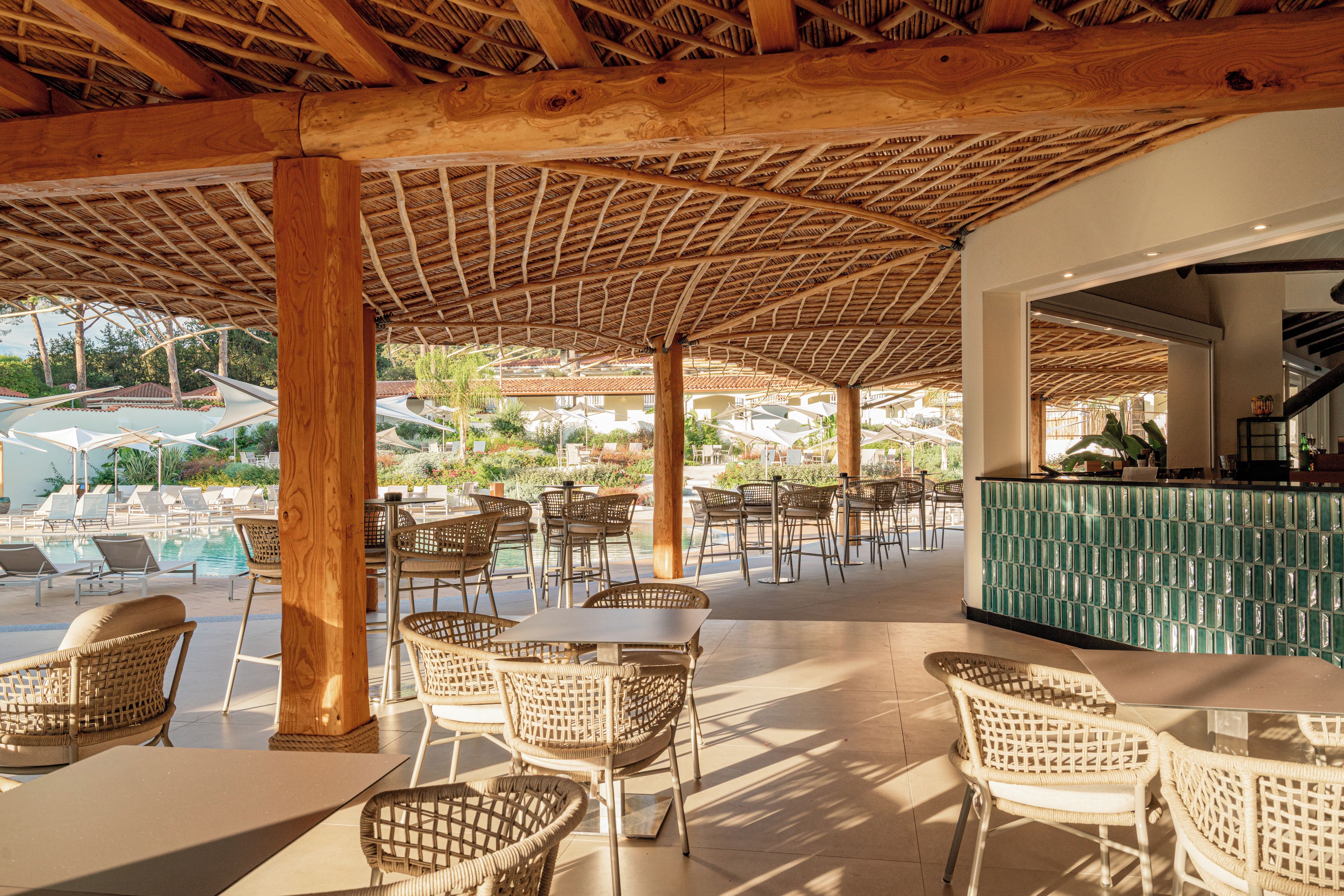 An outdoor seating area with wicker chairs and tables, a pool in the background, and a bar area with a green countertop.