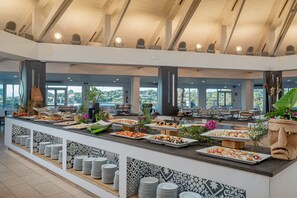 A buffet area with multiple food stations, a variety of dishes, and a view of the outdoors through large windows. - Club Esse Cala Bitta (Arzachena)