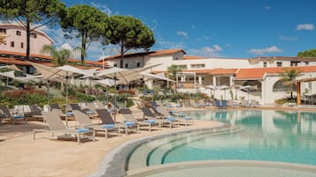 A poolside area with lounge chairs and umbrellas, surrounded by buildings with red-tiled roofs and a clear blue sky.