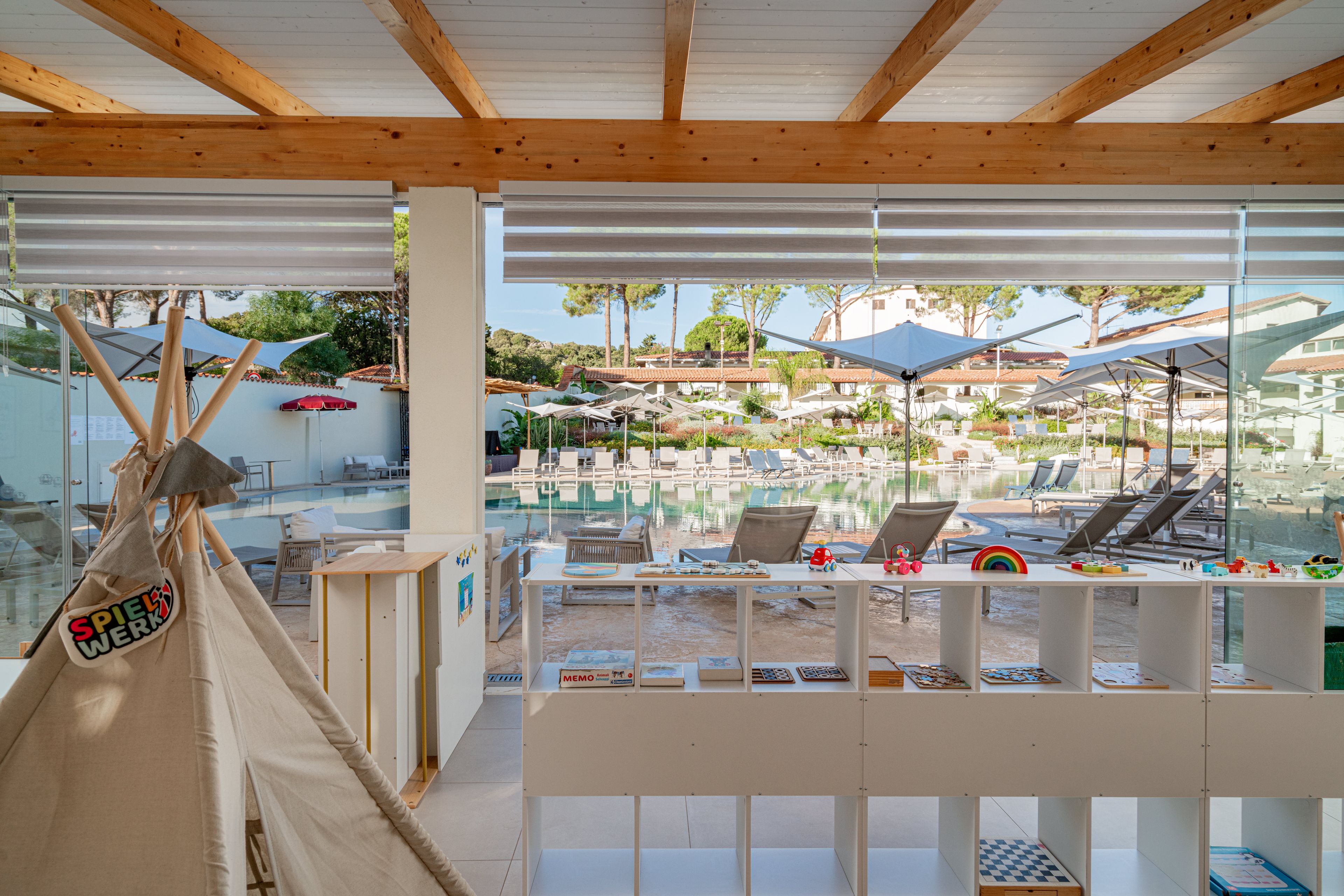 A pool area with lounge chairs and umbrellas, a wooden ceiling, and a view of buildings in the background.