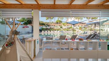 A pool area with lounge chairs and umbrellas, a wooden ceiling, and a view of buildings in the background.